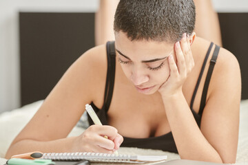 Lovely girl in sexy shirt lying in bed and writing in notebook