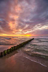 Scenic sunset over Baltic Sea with an old wooden breakwater on the beach.
