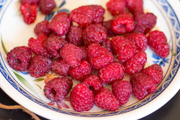 Top view of a white plate, full of juicy red raspberries (Rubus idaeus)