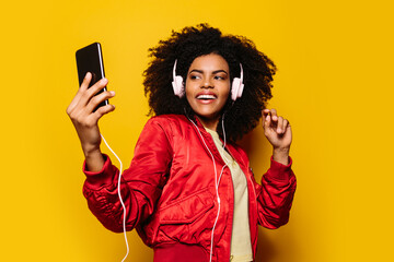 Beautiful afro woman listening to music with white headphones and cellphone