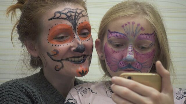 mother and daughter preparing for Halloween celebration and making painted scary face make-up to each other
