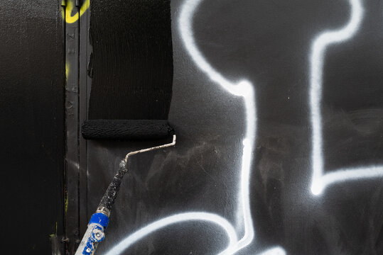 Council worker removing street graffiti by painting over with black paint