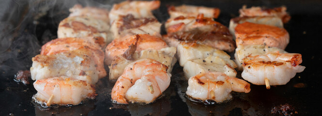 Shrimps and salmon cooking on black barbecue background