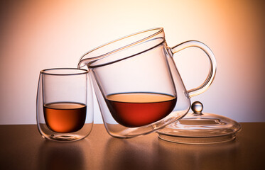 Teapot with a cup on a light colored background. Double-walled glassware. A beautiful composition to show the afternoon tea.