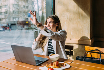 Happy businesswoman using laptop in cafeteria and talking on cellphone