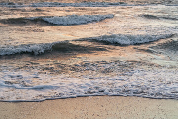 Stormy white glossy waves on sea shore beach close-up with sunset reflection in pastel colors