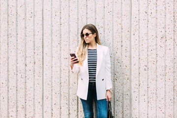 Businesswoman texting on cellphone near a white wall