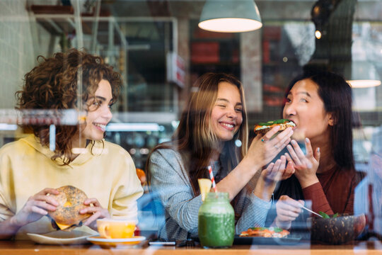 Cheerful woman feeding friend in cafe