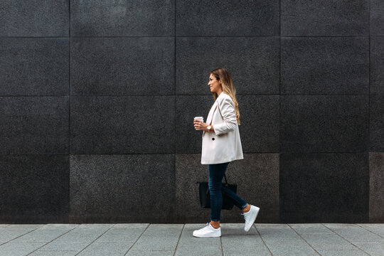 Happy trendy businesswoman walking besides a black wall