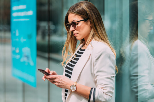 Happy businesswoman in financial area using smartphone outdoors.