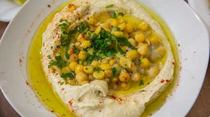 Hummus, traditional Middle eastern Arabic style mashed chickpeas dish, with olive oil, green vegetables and spices, in a white bowl.
Rameh, Northern District, Israel.