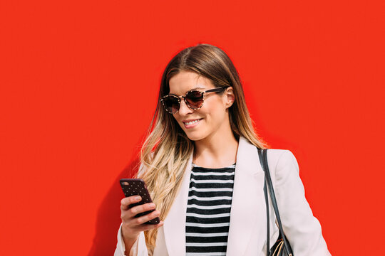 Businesswoman texting on cellphone near a red wall
