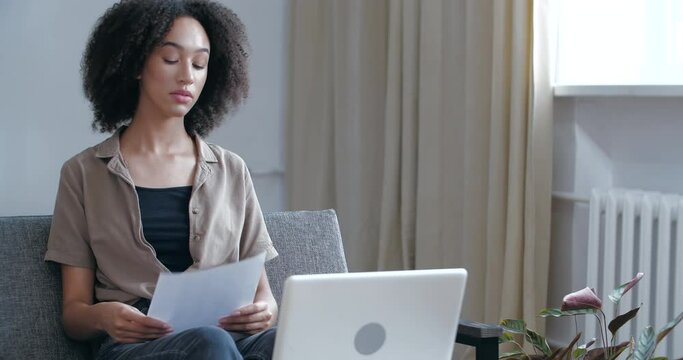 African American girl in casual clothes reads letter results of medical tests, gets bad news, learns about virus disease, feels grief, sadness, desperately clutches head with her hands, pandemic time