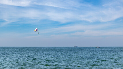 Parasailing on a colorful parachute with boat on sea in blue cloudy summer day. Water vacation