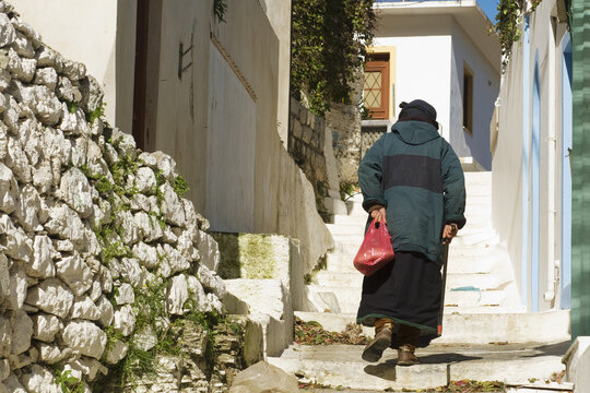 Old Woman Walking Up The Stairs To Olympos Village In Karpathos Island, Greece