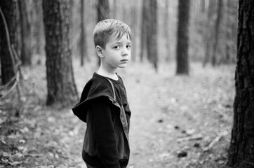 Cute young boy standing among trees in a forest