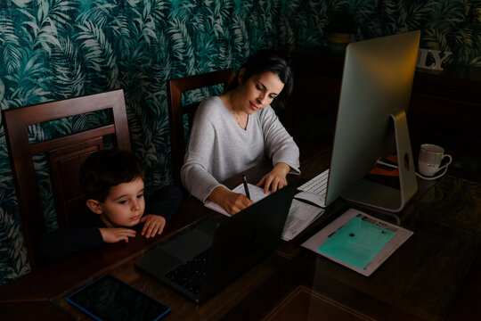 Mother working at home while her bored son look at laptop screen
