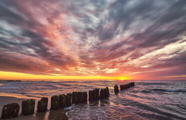 Scenic sunset over the sea with an old wooden breakwater.