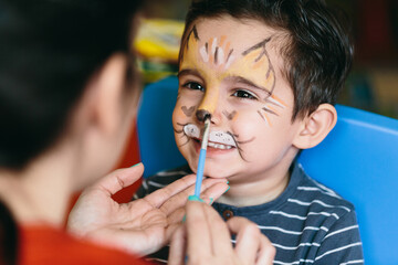 Happy mother putting makeup on her son.