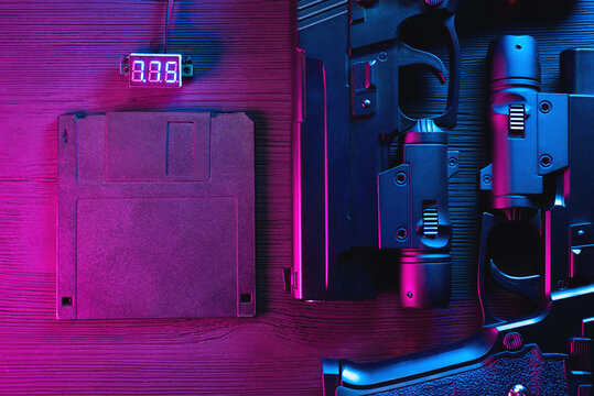 A floppy disk and two toy guns in the neon lights on the table flat lay background.