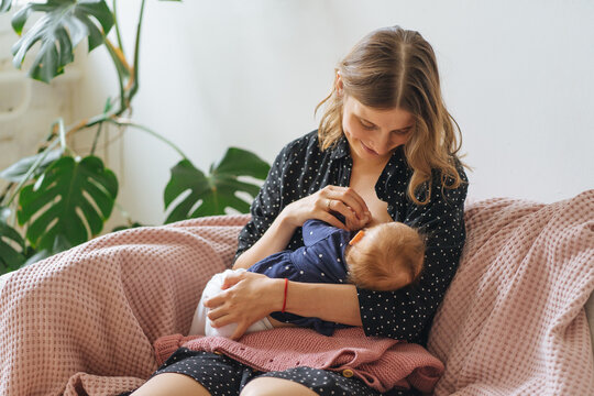young beautiful mother breastfeeds her baby sitting on a sofa