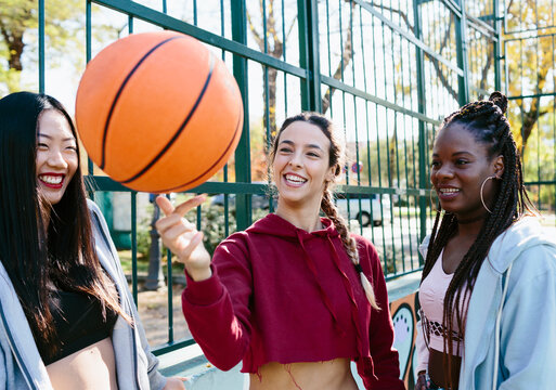 Three women looking at a basketball balancing on a woman's finger