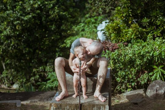 Father bathing child in the garden under a fountain of water