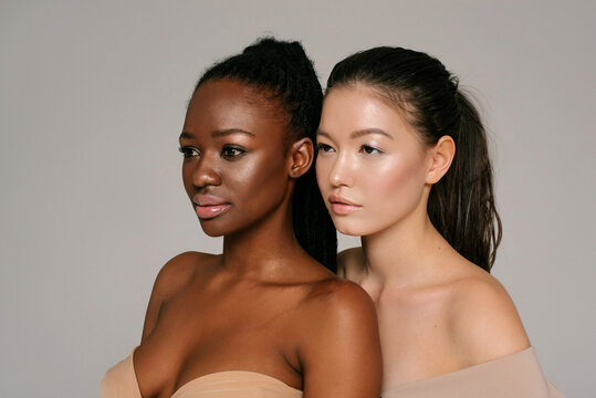Closeup of Asian and black girls on the neutral background looking aside