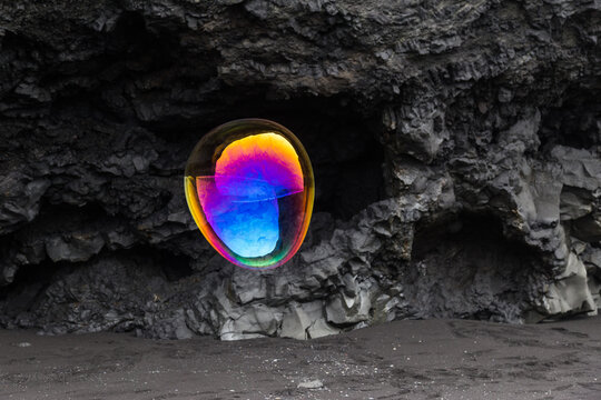 Rainbow coloured soap bubble and black rock