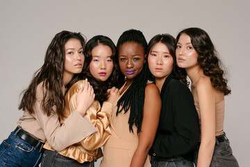 Multicultural shinning girls are sitting together on the grey background