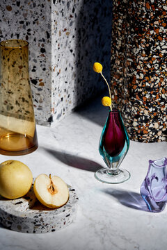 A Still Life Of Colorful Glassware On A Marble Table Top With Asian Pears.