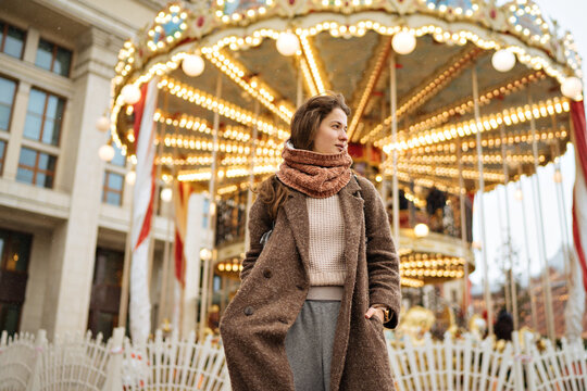 portrait of a charming girl in a brown coat next to a carousel