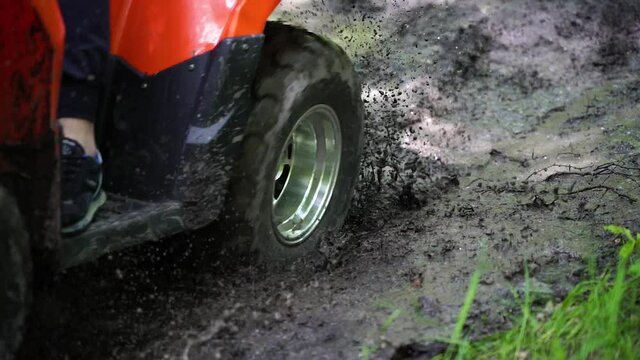 Close up. Slowmotion. The ATV drives into a puddle. Off-road. Dirt from the wheels of the ATV. Dirt from the wheels.