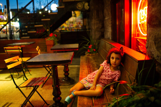 Kid sitting outside a restaurant at night looking at camera