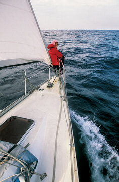 a sailor is sitting on the bow pulpit at sea