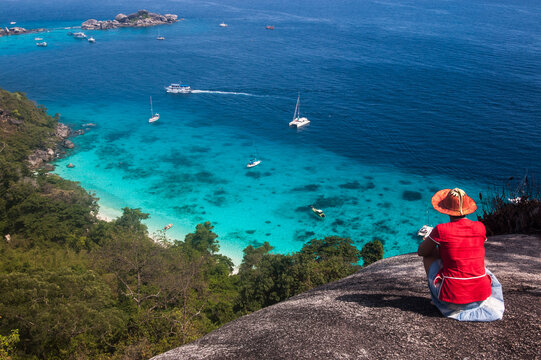 a woman sitting on a high rock in the similan islands overlooking the ocean