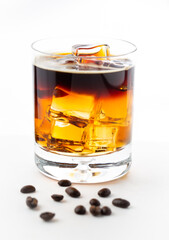 Glass of iced coffee with coffee beans spread around it on white background