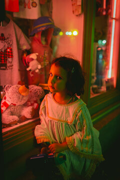 Girl sitting by a neon lighted store window