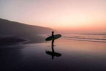 Unrecognizable man with surfboard standing on wet sandy beach at the ocean
