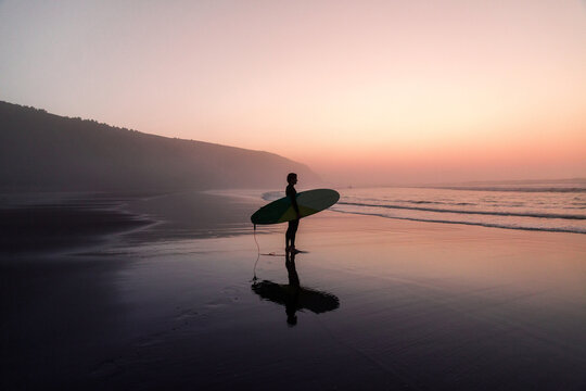 Unrecognizable man with surfboard standing on wet sandy beach at the ocean - Powered by Adobe