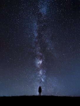 Silhouette of unrecognizable person standing under cosmic sky at night