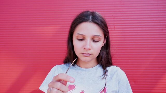 Portrait of a girl taking off a black balaclava from her face on a red background. Identity disclosure, rejection of anonymity. 