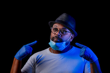 Black man shows how not to use a face mask wearing blue gloves with a black background.