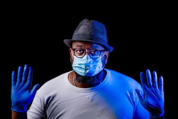 Black man with blue gloves and face mask says stop with black background.