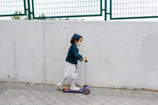 Kid with protective mask rides her scooter in the street