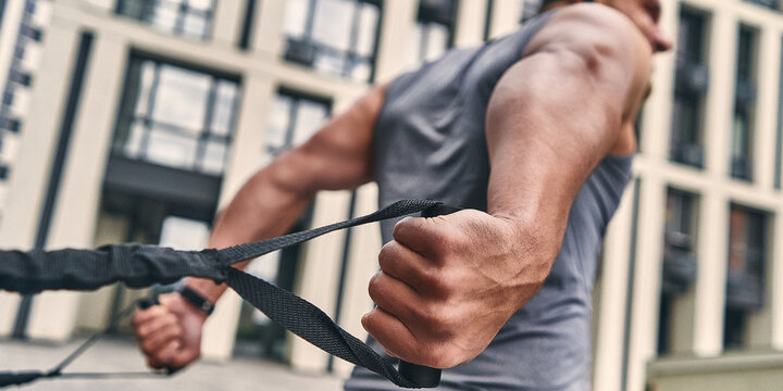 Focus on the strong muscular back of a man exercising outdoors with loops. Sport concept