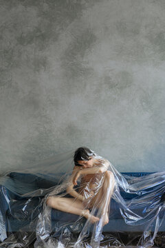 concept photo. The girl is lying under a cellophane film on the sofa