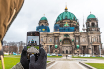 Hands with gloves holding a smartphone and taking a picture of the Berlin Cathedral on a winter day