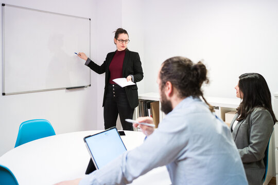 Young female manager standing near whiteboard and explaining marketing strategy of business project to focused colleagues during presentation in contemporary coworking room
