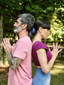Side view of tranquil man and woman practicing yoga in Tadasana while standing back to back with closed eyes and Namaste hands in park